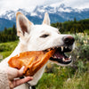 A dog eating a Pig Ear Dog Treat (25 Pack) in front of a mountain, made by Best Bully Sticks.