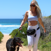 A woman walking her dog on a beach carrying the BEST Neoprene Fanny + Crossbody - Black by Best Bully Sticks.