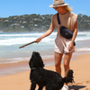 A woman with a dog on a beach carrying The BEST Neoprene Fanny + Crossbody - Black by Best Bully Sticks.