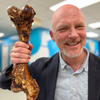 A bald man holding up a Monster Femur Bone from Best Bully Sticks in a lab.